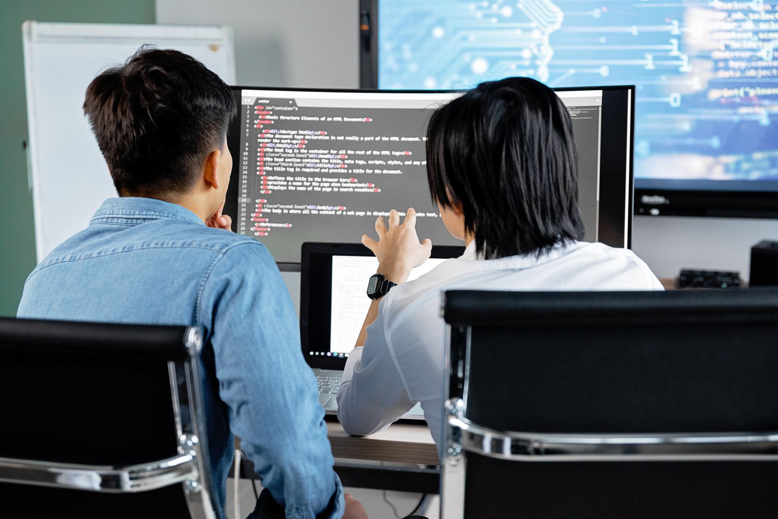 Software developers collaborating at a workstation with code on screen